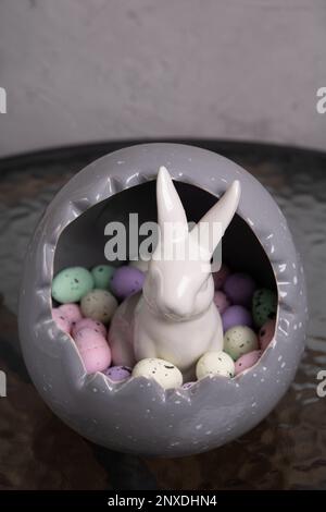 photo in a large gray egg lies a lot of colorful decorative small eggs and a white rabbit Stock Photo