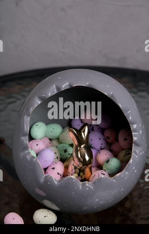 photo a lot of colored Styrofoam eggs lying in a large gray egg and inside is a rabbit on a glass table Stock Photo