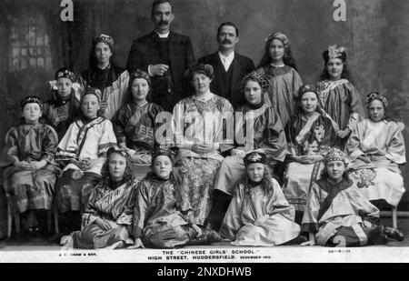 The Far East comes to West Yorkshire, England, UK: girl pupils of the ‘Chinese Girls’ School’ in Huddersfield High Street sit in December 1912 for a group portrait with their teachers and a clergyman while exotically dressed in Chinese costume typical of the era.  Monochrome vintage postcard published by Huddersfield and Sheffield photographers, John Edward Shaw & Son. Stock Photo