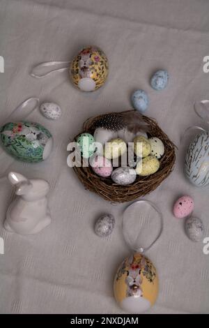 photo on a white tablecloth with lots of decorative colored eggs and a white Easter bunny and a nest of colored quail eggs on the table Stock Photo