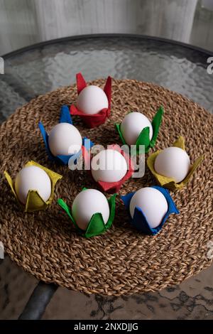 photo white eggs lying in colorful containers on a wicker stand on a glass table Stock Photo