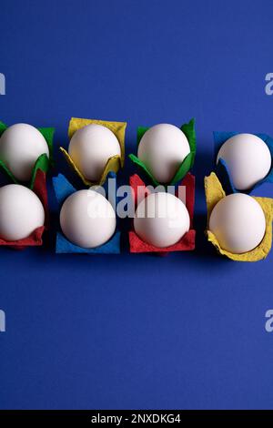 photo eight white hen eggs in colored packages on a blue background Stock Photo