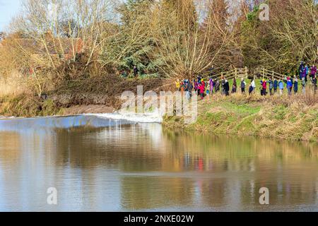 Crowds watching the 4 star Severn Bore on 23/2/2023 break against the bank of the River Severn at Minsterworth, Gloucestershire, England UK Stock Photo