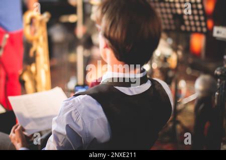 Orchestra jazz musician during performance, rehearsal sound recording, saxophonist player holding musical notes on paper sheet, before the concert, mu Stock Photo