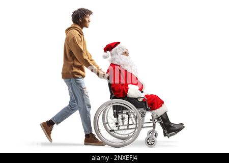 Full length profile shot of an african american young man pushing a santa claus in a wheelchair isolated on white background Stock Photo