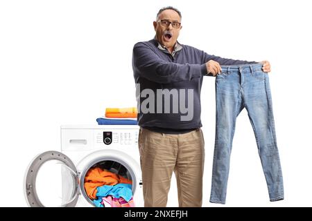 Shocked mature man taking out a pair of jeans from a washing machine isolated on white background Stock Photo