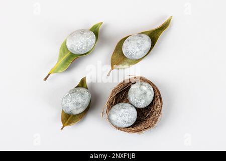 Minimal ecological Easter concept with dried flowers. Gray eggs on dry magnolia leaves and in a brown nest of twigs on a gray background Stock Photo