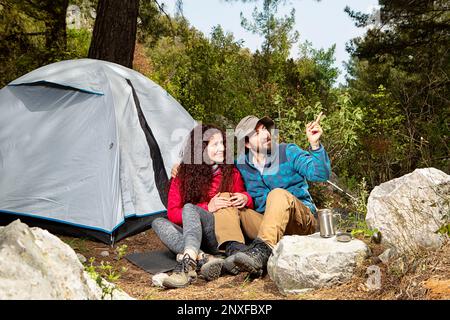 Young tourist couple travellers with tent shelter sitting in nature, using smartphone Stock Photo