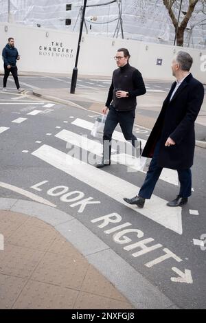 With the former US Embassy being refevloped into a luxury property in the background, pedestrians cross the road on a zebra crossing in Grosvenor Square in Mayfair, on 27th February 2023, in London, England. The Chancery Rosewood, in partnership with real estate developer Qatari Diar, is to open in 2024 at the location of the Grade II listed former U.S. Embassy building. Stock Photo