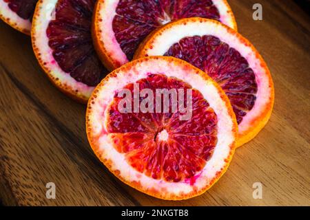 Closeup of Blood Orange Slices on a Wooden Cutting Board: Sliced citrus fruit with whole blood oranges on the side Stock Photo
