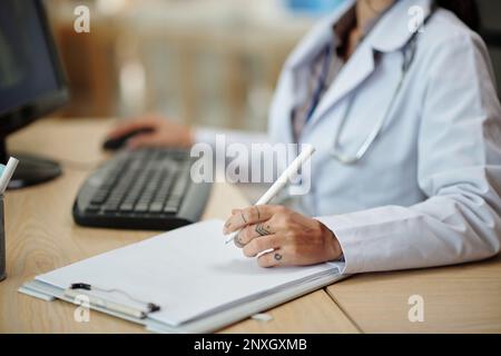 Cropped image of physician checking patients medical history in database on computer and taking notes Stock Photo