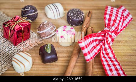 Variety of luxury chocolate pralines truffles with holiday decorations, red and white ribbon on wood. Stock Photo