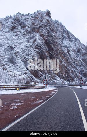 Bad Kreuznach, Germany - February 8, 2021: Road leading to a railroad crossing in front of part of Rotenfels covered in snow on a cold, gray winter da Stock Photo