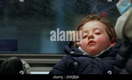 One cute little boy sleeping inside subway train. Child asleep on mother lap closeup face with wagon passing by in background Stock Photo