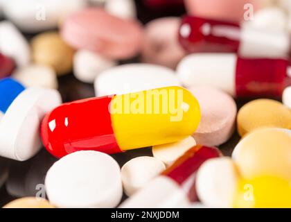 red and yellow pill over several colored pills , close up on a black background Stock Photo