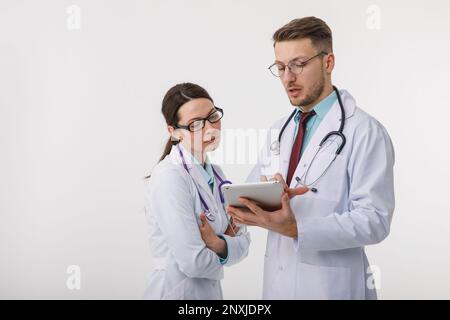 Young doctors, a man and a woman, study data on a tablet. Isolated on a white background. Technology to help medicine concept. Stock Photo