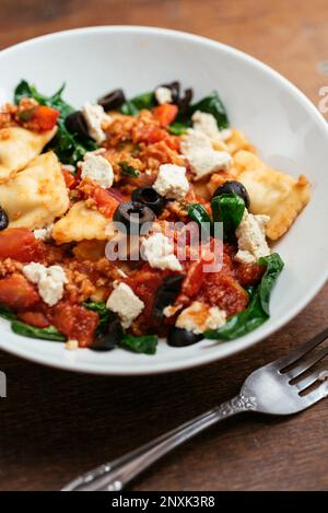 Bowl with vegan ravioli with spinach, TVP, olives, a tomato sauce and home made vegan feta. Stock Photo