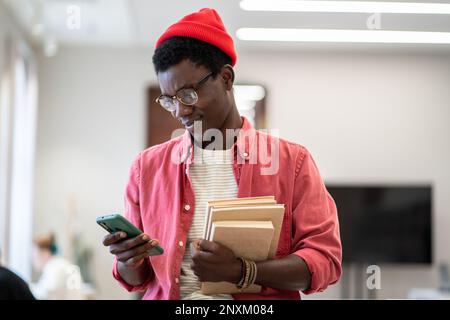African American man teacher standing in library using scheduling app on mobile device Stock Photo