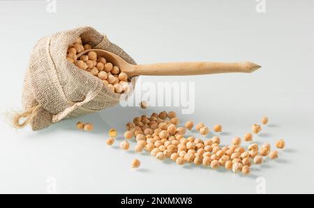 A jute decorative bag with grains of chickpeas on a light background. A wooden spoon sticks out of the peas Stock Photo