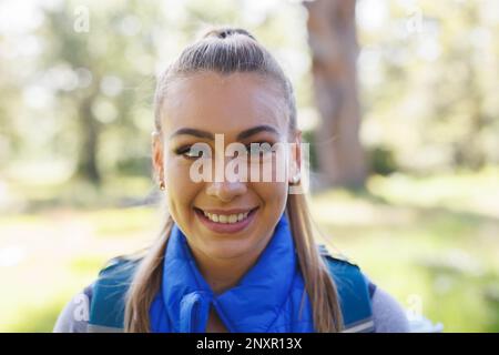 Portrait of attractive blonde caucasian woman trekking in sunny forest, smiling, copy space Stock Photo