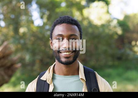 Portrait of happy african american man trekking in forest with backpack, smiling, copy space Stock Photo