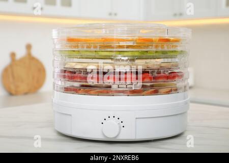 Dehydrator machine with different fruits and berries on white marble table in kitchen Stock Photo