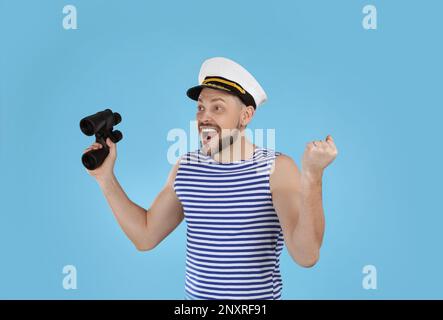 Happy sailor with binoculars on light blue background Stock Photo