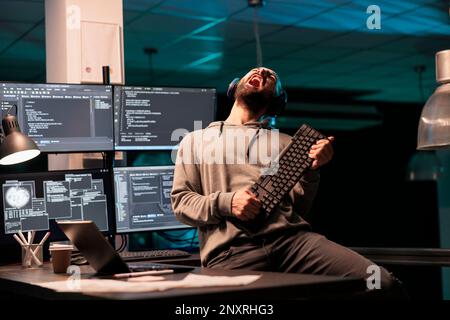 Database programmer playing guitar with keyboard, writing code with cloud computing and programming html source. Cheerful smiling developer having fun and acting silly in office. Stock Photo