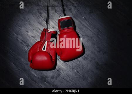 Pair of red boxing gloves hanging in spotlight on grey stone background. Space for text Stock Photo
