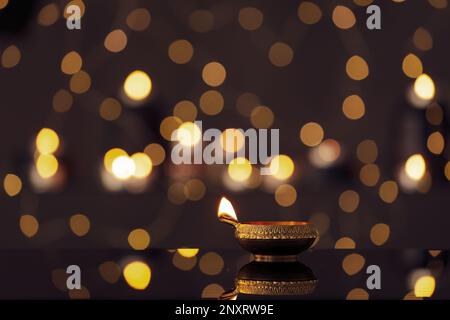 Lit diya on table against blurred lights, space for text. Diwali lamp Stock Photo