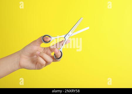 Hairdresser holding professional thinning scissors on yellow background, closeup. Haircut tool Stock Photo