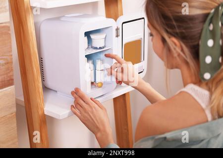 Woman taking cosmetic product from mini fridge indoors, closeup Stock Photo