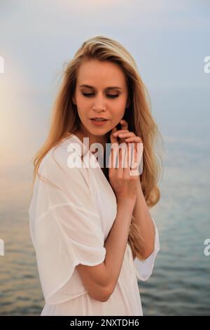 Beautiful young woman near sea in evening Stock Photo