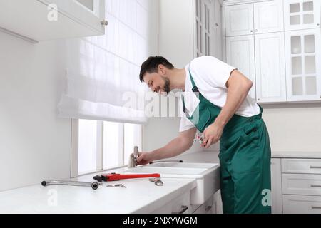 Professional plumber fixing water tap in kitchen Stock Photo