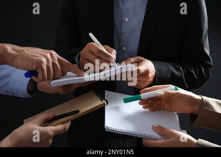 Man signing autograph in notebooks on dark background, closeup Stock Photo