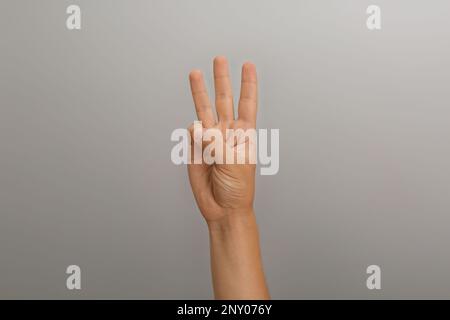 Teenage boy showing three fingers on light grey background, closeup Stock Photo