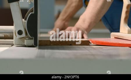 Close-up of man cutting board on machine. Creative. Carpenter processes wooden board on machine. Industrial processing and trimming of wooden boards w Stock Photo