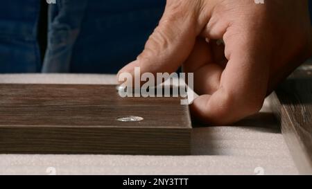 Close-up of man inserting screws into wooden board. Creative. Carpenter screws screws into holes of wooden board. Screwing screws into wooden board. Stock Photo