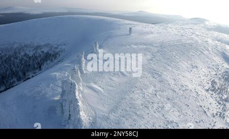 Landscape in sub-zero temperatures from above. Clip.Snowy empty mountains with frozen hills and trees are visible against a bright sky. High quality F Stock Photo