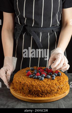 A female chef decorates a homemade carrot cake with fresh berries on a dark background. selective focus Stock Photo