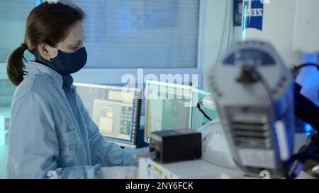 The working process. Stock footage. A woman in a special uniform in a dressing gown and a mask works at a special complex production at a keyboard wit Stock Photo