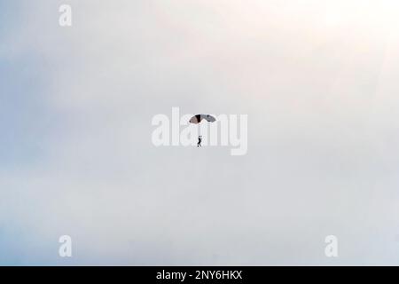 Skydiver with a blue little canopy of a parachute on the background a blue sky and white clouds Stock Photo