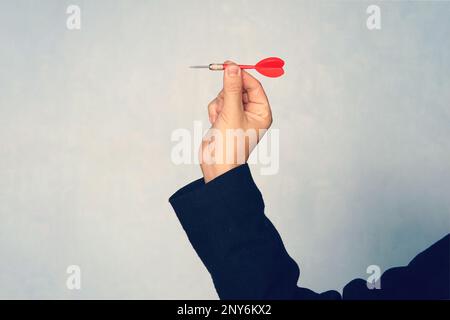 Businessman holding a dart aiming at the target - business targeting, aiming, focus concept. hand in jacket throws a dart to the side. hit the target. Stock Photo