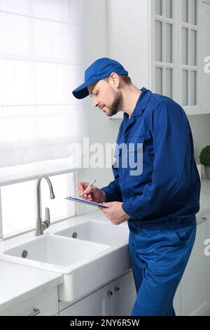 Professional plumber with clipboard checking water tap in kitchen Stock Photo