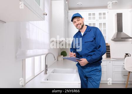 Professional plumber with clipboard checking water tap in kitchen Stock Photo