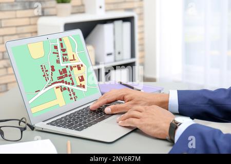 Man analyzing cadastral map on laptop at table, closeup Stock Photo