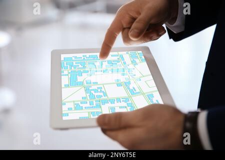 Man analyzing cadastral map on tablet indoors, closeup Stock Photo