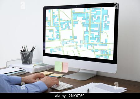 Man analyzing cadastral map on computer at table, closeup Stock Photo