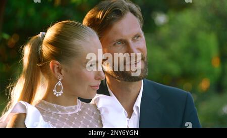 Beautiful bride with groom in a city park on a green blurred background. Action. Man and woman newlyweds during video shooting outdoors Stock Photo