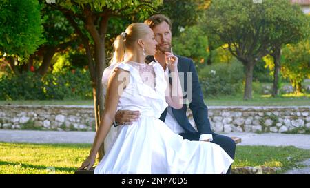 Beautiful bride with groom in a city park on a green blurred background. Action. Man and woman newlyweds during video shooting outdoors Stock Photo